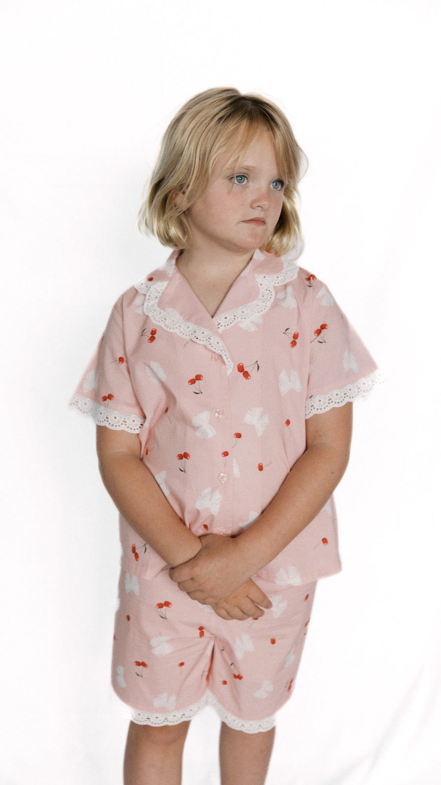 Young girl wearing a pink pajama set with lace details on a white background
