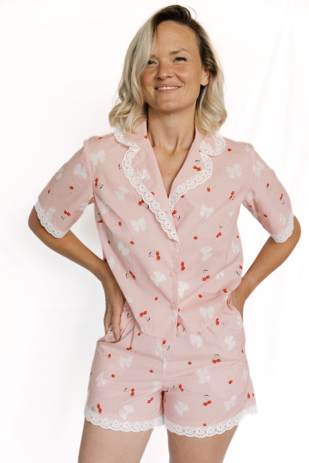 Woman wearing a pink pajama set with cherry pattern on a white background