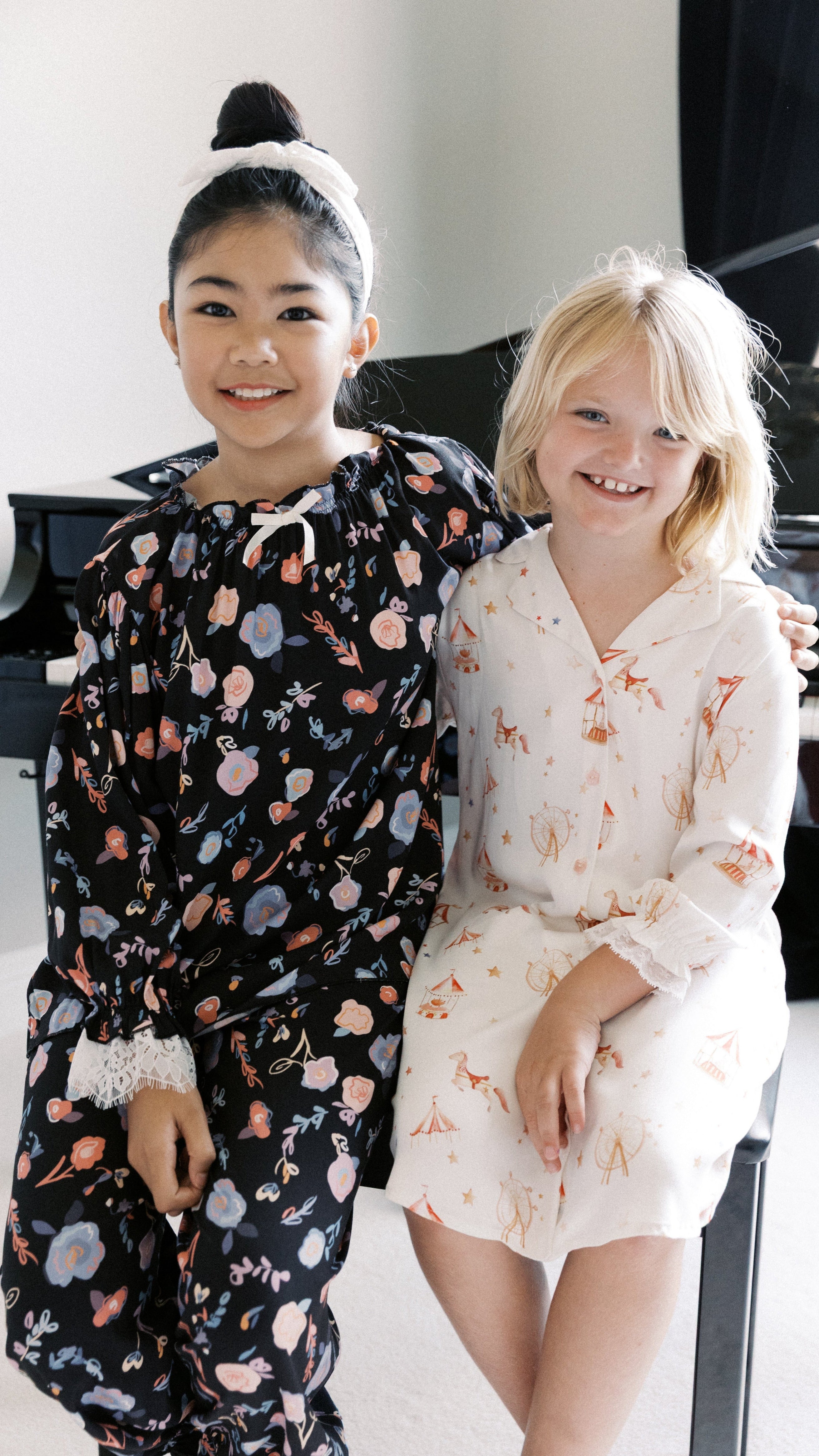 Two young girls in floral pajamas sitting in front of a piano.