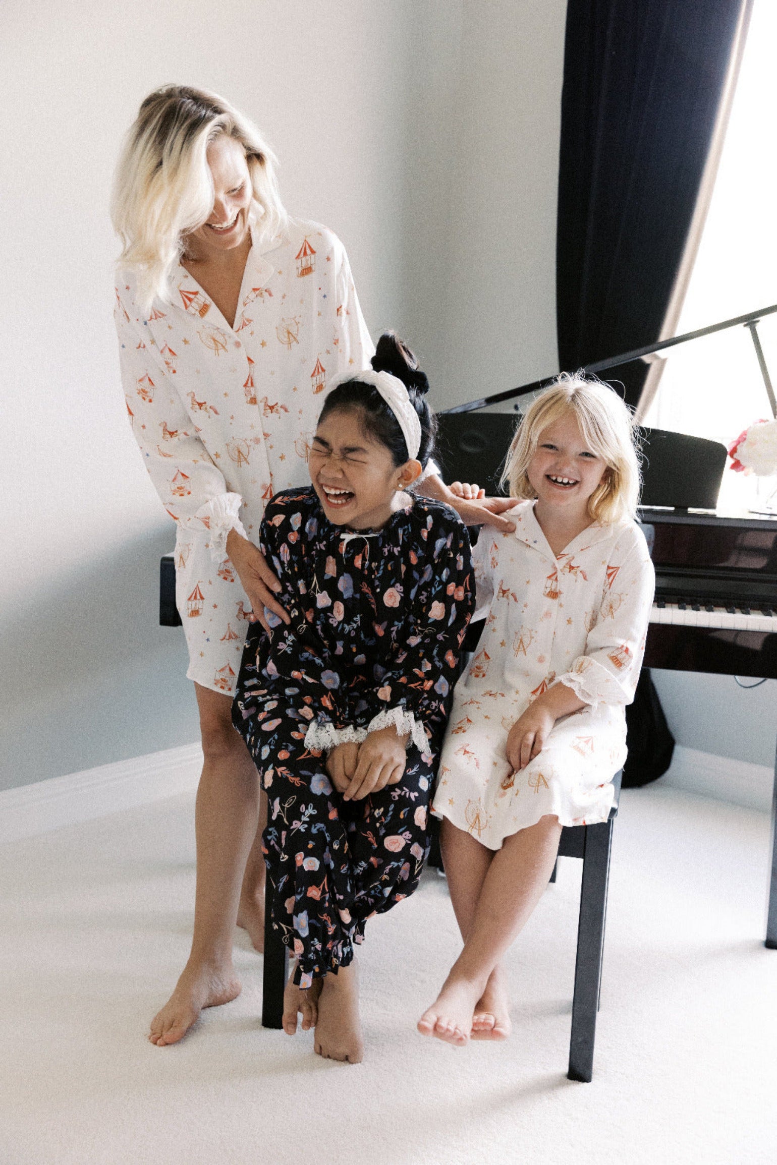 Woman and two children in matching pajamas sitting on a piano bench.