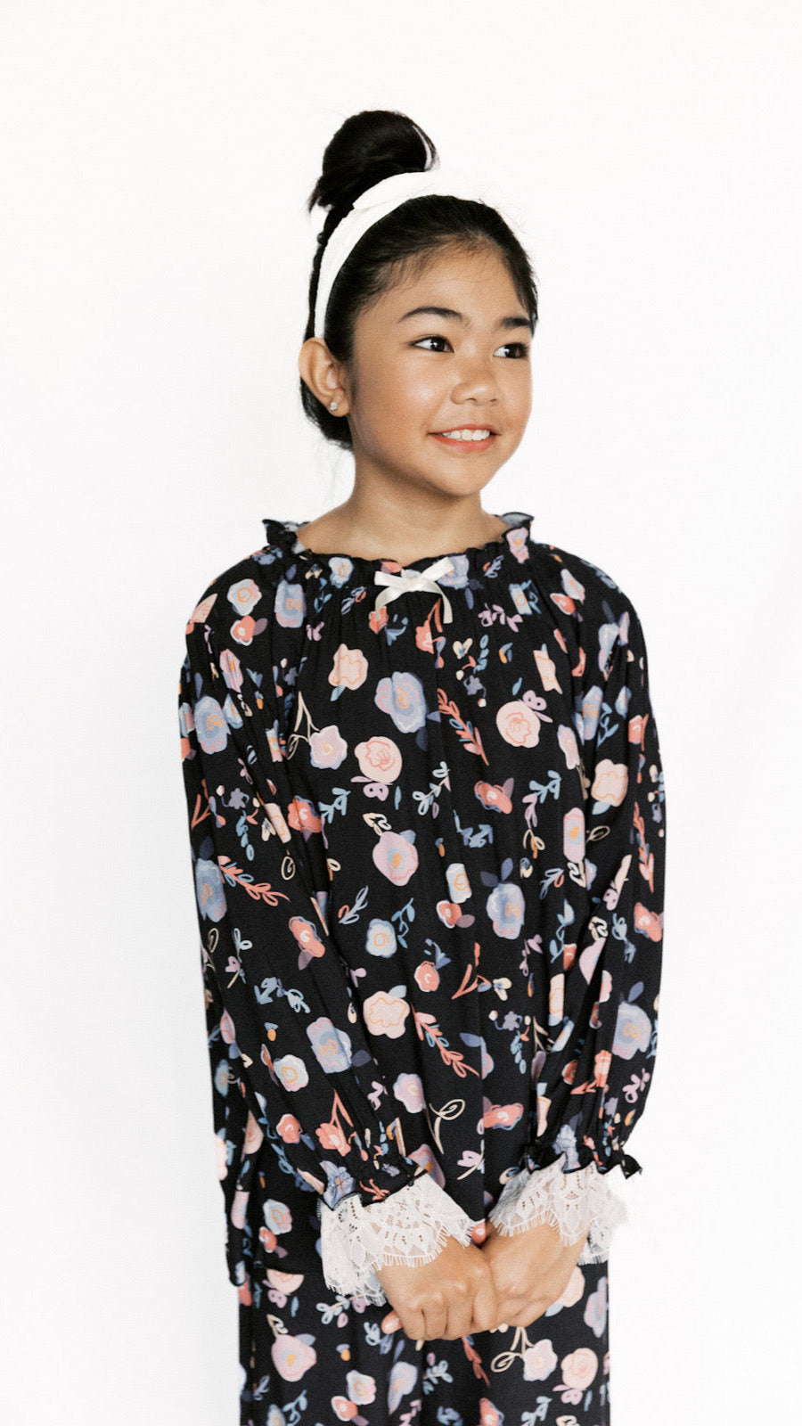 Young girl wearing a black floral patterned PJs with white lace trim on a white background
