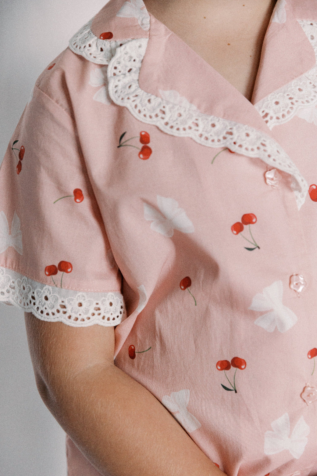 Pink pajama top with cherry pattern and lace trim on a neutral background